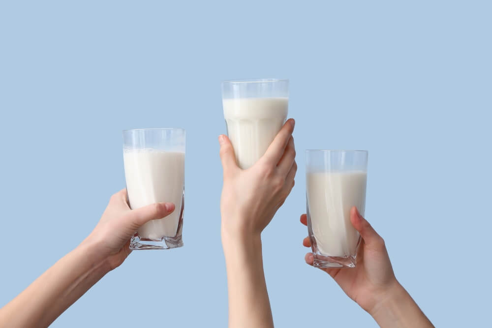 Tri roke dvigajo v zrak tri kozarce z veganskimi nadomestki mleka