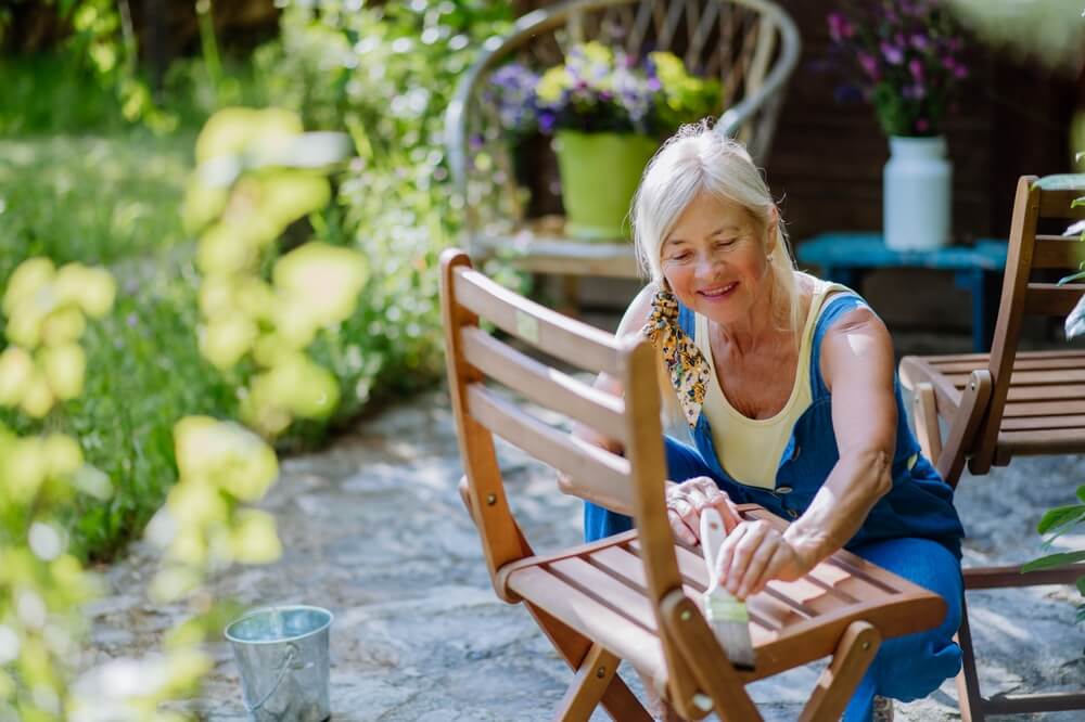 Gospa srednjih let obnavlja zaščito lesa na vrtnem stolu